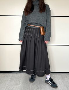 a woman standing in front of a white wall wearing black and grey clothing with her hands on her hips