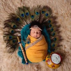 a baby wrapped in a yellow blanket next to a can and peacock tail with feathers on it's head