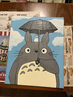 a painting of a totoro holding an umbrella on top of a wooden table