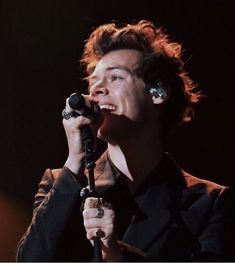 a young man holding a microphone in his right hand and singing into the microphone on stage