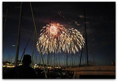 fireworks are lit up in the night sky over boats and yachts at a marina