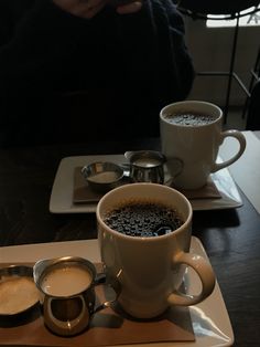 two cups of coffee sit on a plate with spoons next to it and another cup is in the foreground