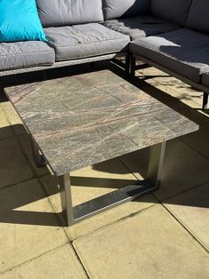 a table sitting on top of a cement floor next to a gray couch and blue pillows