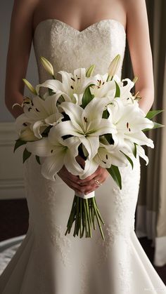 a bride holding a bouquet of white lilies in her wedding dress and looking at the camera