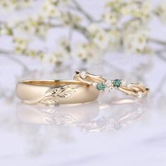 two gold wedding rings with green and white stones on them, sitting next to each other