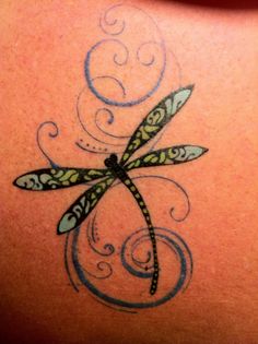 a dragonfly tattoo on the back of a woman's shoulder, with swirls and