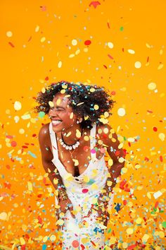 a woman in a white dress is surrounded by confetti and streamers on an orange background