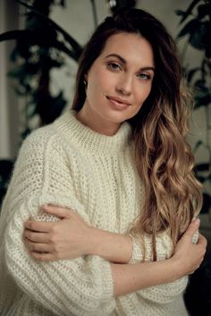 a woman with long hair wearing a white sweater and holding her arms crossed in front of her chest