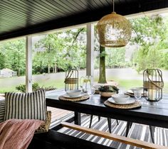 a table with plates and cups on it in front of a covered porch that has trees