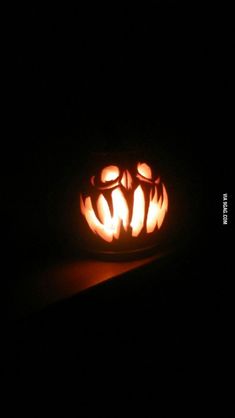 a carved pumpkin sitting on top of a table in the dark with its eyes open