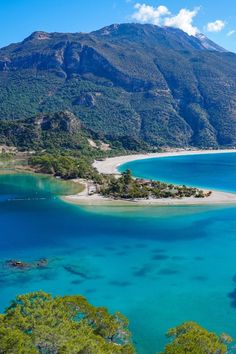 an island in the middle of blue water surrounded by mountains and greenery on either side