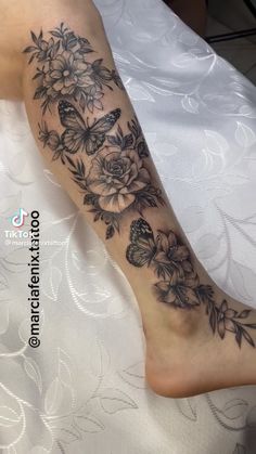 a woman's foot with flowers and butterflies tattoo on her left leg, sitting on a bed