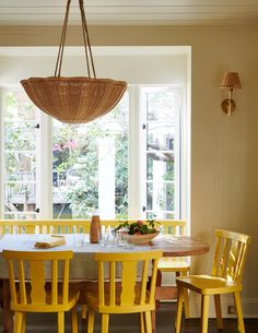 a dining room table with yellow chairs and a basket hanging from the ceiling