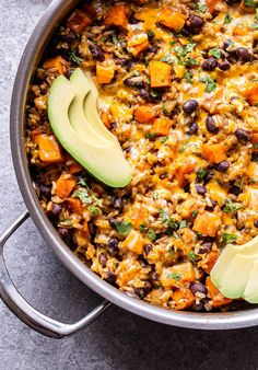 a pot filled with black beans, rice and avocado wedges on the side