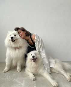 a woman sitting on the floor with two white dogs and one is hugging her head