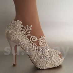 a woman's white high heeled shoe with lace and flowers on the side