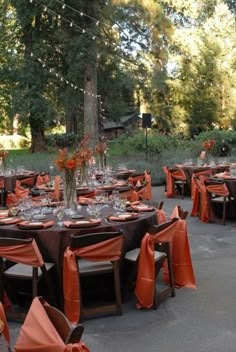 an outdoor dining area with tables and chairs covered in orange cloths, decorated with flowers