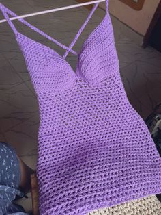 a purple crocheted top hanging on a clothes line with someone's feet in the background