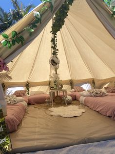 a bed with pink sheets and pillows under a large white canvas tent that is decorated with greenery