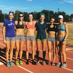 four women standing on a track posing for the camera with their arms around each other