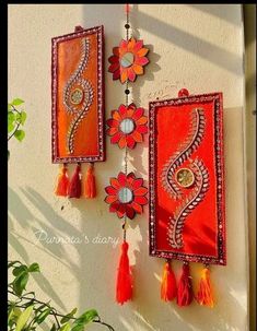 two orange and red wall hangings with tassels attached to the side of a building