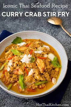 a white bowl filled with curry crab stir fry on top of a blue towel next to a spoon