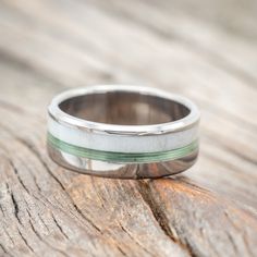 a wedding band that is sitting on top of a piece of wood, with a green stripe in the middle