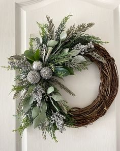 a wreath is hanging on the front door with greenery and pineconis around it