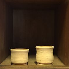 two white pots sitting on top of a shelf in a wooden box next to each other