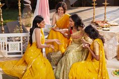 three women in yellow sari sitting on a bench talking to each other and laughing