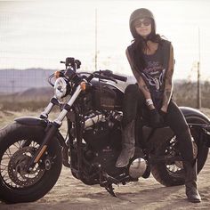 a woman sitting on top of a motorcycle in the dirt with her legs crossed and wearing boots