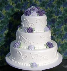 a three tiered white cake with purple flowers on it