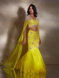 Yellow sleeveless embellished blouse paired with a fitted fishtail skirt & georgette layer featuring hand-embellished champagne & silver daffodils & paired with a net cape hand embellished with pearls & glass beads & tassels.From Shloka Khialani's Winter Sun collection.DELIVERY TIMEPlease allow 6-8 weeks for your outfit to arrive.FABRIC DETAILSGeorgette, NetProfessional cleaning only. Tassel Skirt Outfit, Latest Bridal Lehenga Designs, Beads Tassels, Haldi Outfits, Bridal Lehenga Designs, Haldi Outfit, Latest Bridal Lehenga, Tassel Skirt, Lehenga Style