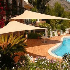 an outdoor swimming pool with patio furniture and umbrellas in the shade, surrounded by flowers