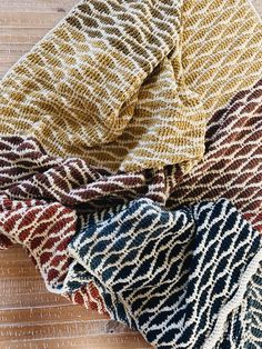 three knitted scarves sitting on top of a wooden table