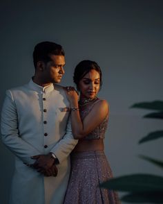 a man and woman standing next to each other in front of a wall with plants