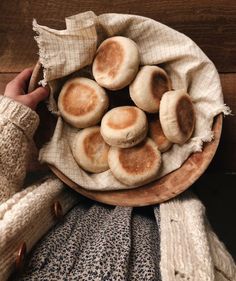 a wooden bowl filled with mushrooms on top of a table next to a person's hand