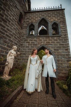 two people standing next to each other in front of a stone building with statues on either side