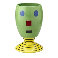 a green and yellow vase with a face on it's side, in front of a white background