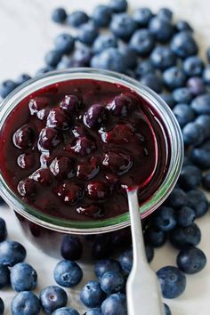 a glass bowl filled with blueberry sauce next to fresh blueberries and a spoon