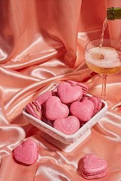 pink heart shaped cookies in a bowl next to a glass of wine