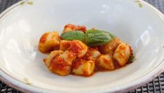 pasta with tomato sauce and basil in a white bowl on a black tableclothed surface