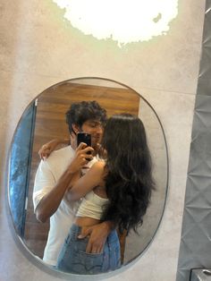 a man and woman standing in front of a mirror taking a selfie with their cell phone