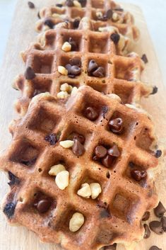 two waffles with chocolate chips and nuts on them sitting on a cutting board