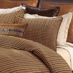 a bed covered in brown and white plaid comforter next to a night stand with two pillows