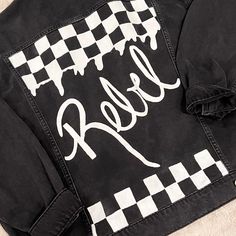 This listing is for an oversized hand-painted upcycled black jean jacket. Size M On the back you will find a hand-painted white dripping checkered print with the word Rebel painted in white. On the front you will find two patches - a smiley face and a checkered heart. Fundraiser Ideas, Checkered Jacket, Checkered Print, Checker Print, Printed Jeans, Smiley Face, White Painting