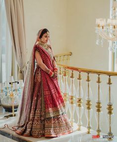 a woman in a red and gold bridal gown standing on a stair case next to a chandelier