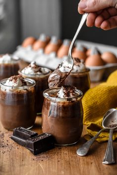 someone is spooning chocolate pudding into small glasses with whipped cream on top and other desserts in the background