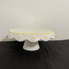 a white cake plate with yellow trim and daisies on the edge, sitting on a black table