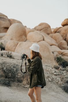 a woman standing in the desert holding a camera and taking pictures with her hat on